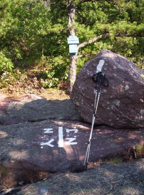 The New York - New Jersey state line, marked by white painted abbreviations and a line on a large rock, with a blaze and trail register off the side of the trail